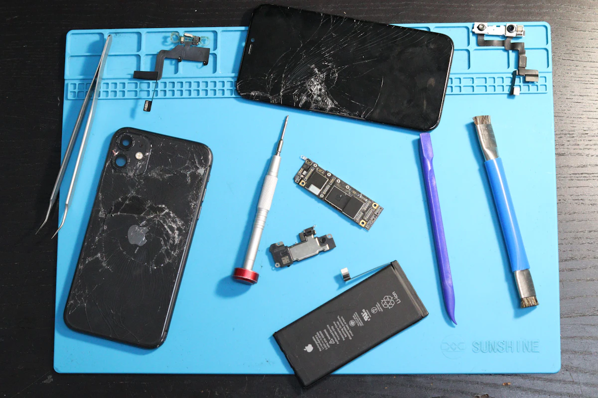 Opened phones, a battery and repair tools on a work mat